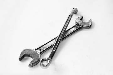 A pair of crossed metal wrenches on a clean white surface.